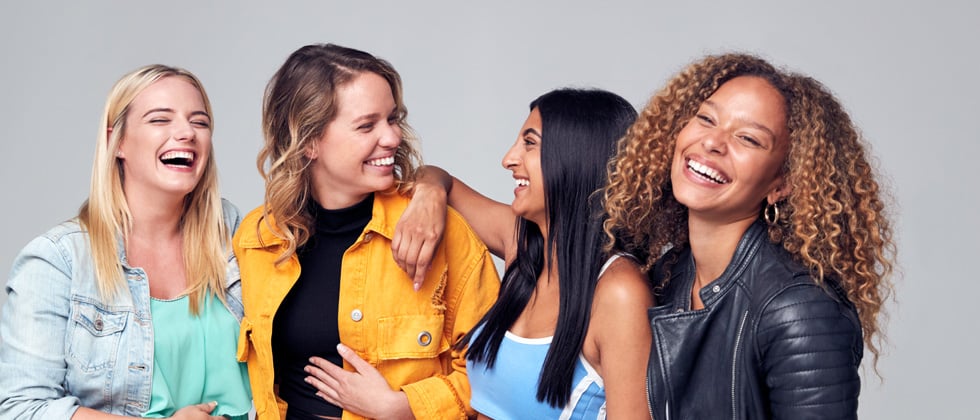 A group of young women standing laughing while standing close together