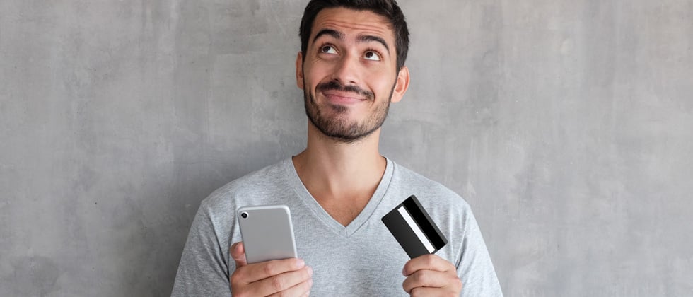A guy on his phone looking a credit card thinking about buying something