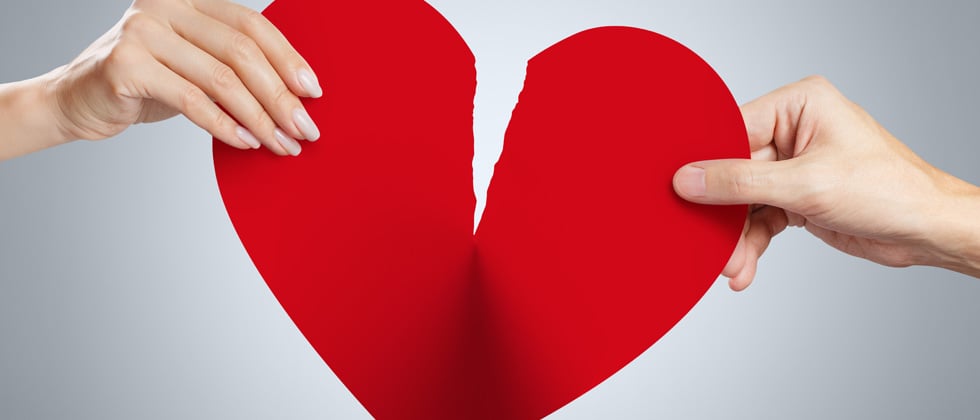 A big paper heart being riped by two people pulling at it