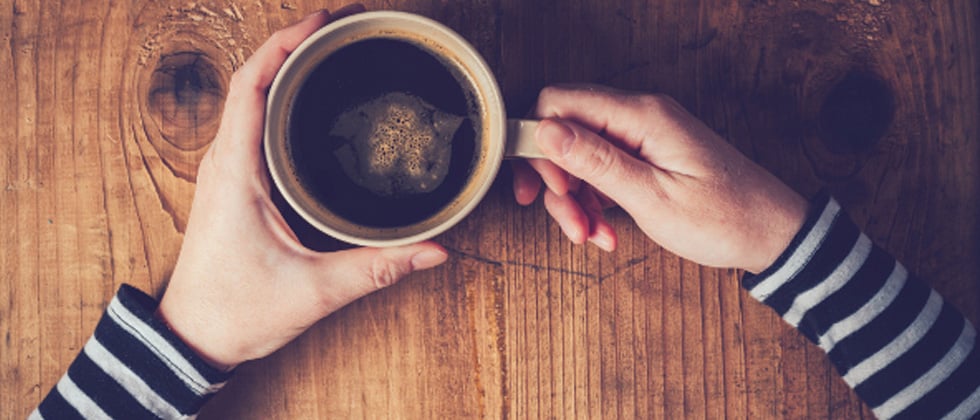 Someone sitting alone holding a black cup of coffee