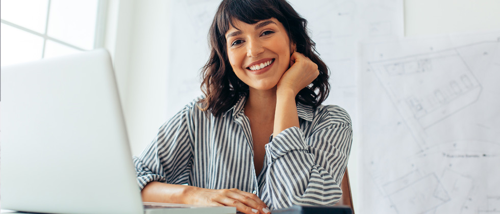 A woman sitting at her desk in front of her laptop smiling