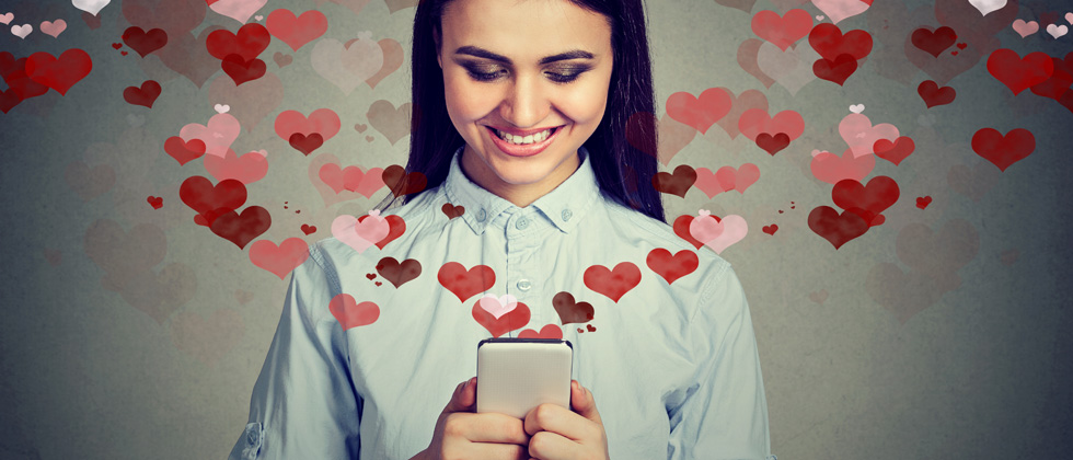 A woman smiling & holding her phone with dozens of hearts flying out of it
