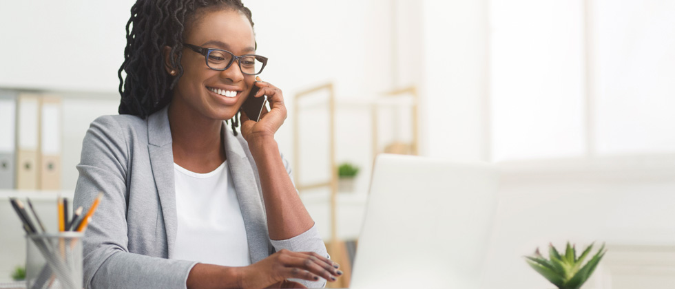 A woman talking on the phone while working on her laptop at her desk