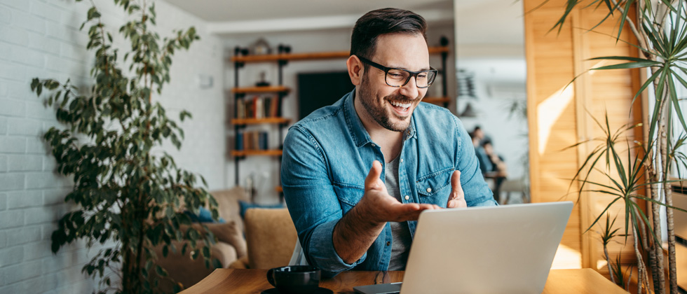 A guy sitting at his desk wiht his laptop smiling on a video call