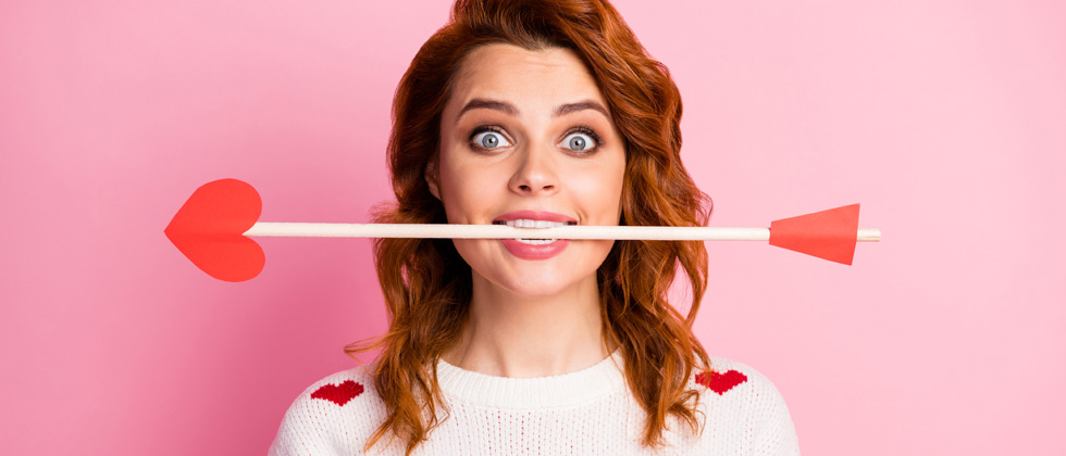 A woman in a heart sweater with cupid's arrow between her teeth