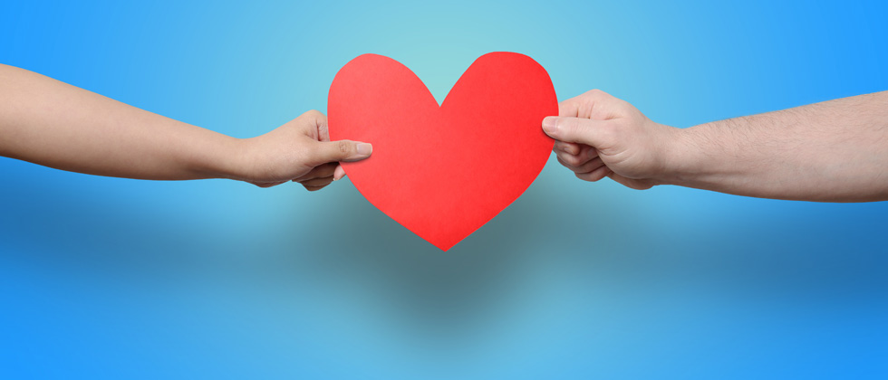 Two people grabbing at a big paper heart at each end
