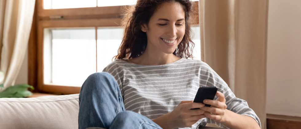 A woman sitting on her couch smiling while holidng her cell phone