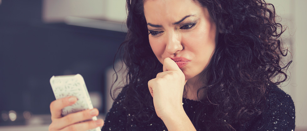 A woman looking annoyed and confused at her cell phone