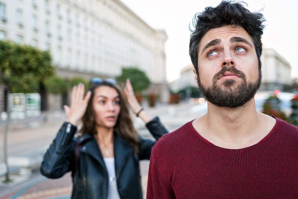 A woman and a man are standing on the street and seem to argue. The woman is looking angry and the man is annoyed.