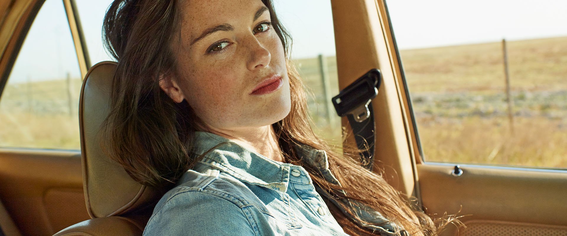 A woman sitting in a car, looking directly at the camera with a serious face.