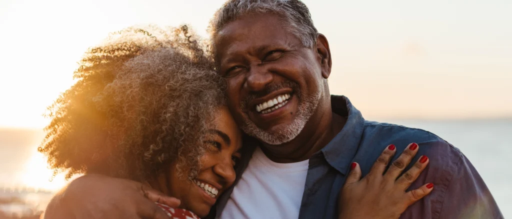 Happy Black senior couple embracing and smiling at sunset.