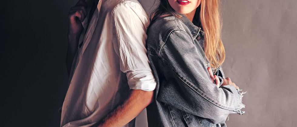 A couple with their backs to each other & one is looking over to the other