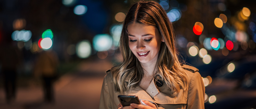 A woman standing in the street at night looking down at her phone