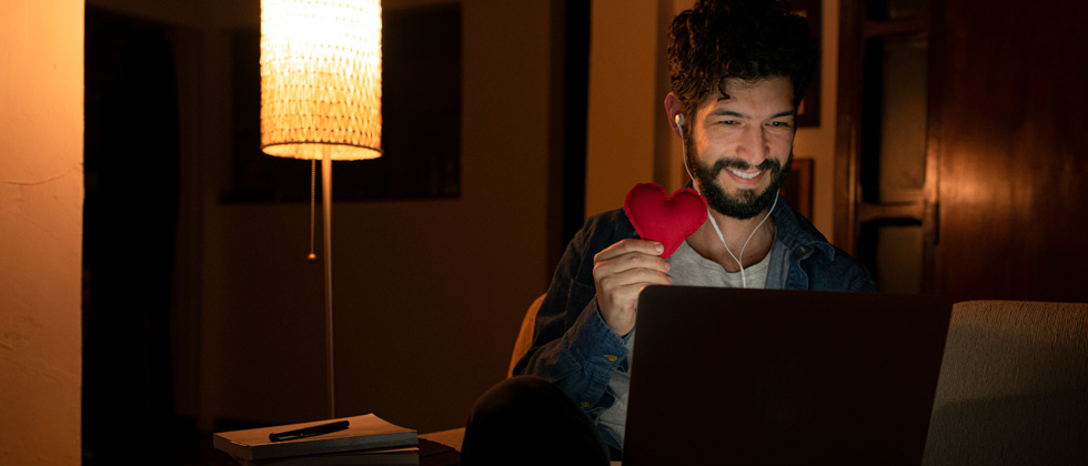 Man video chatting and showing his date a cutout heart