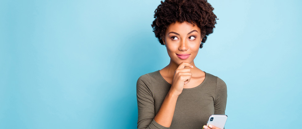 Young woman standing holding her phone pondering about something
