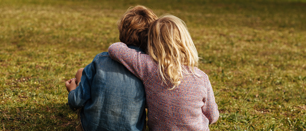 Two kids sitting with their arms around each other looking out