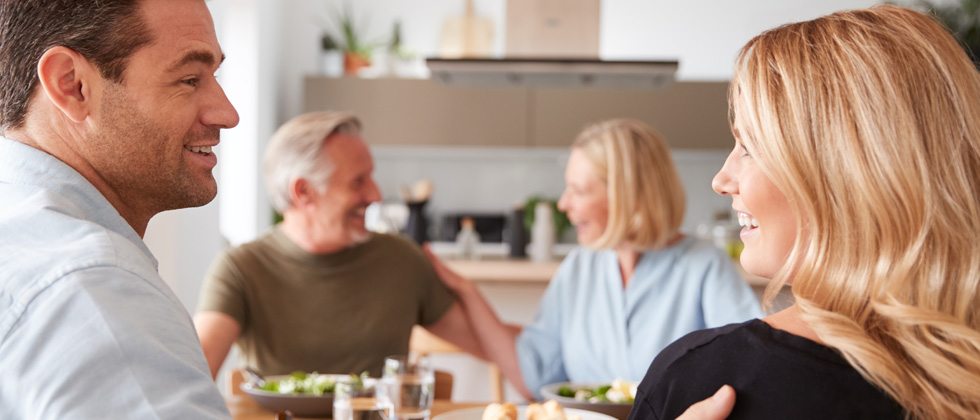 A couple sitting and laughing at dinner across from their parents