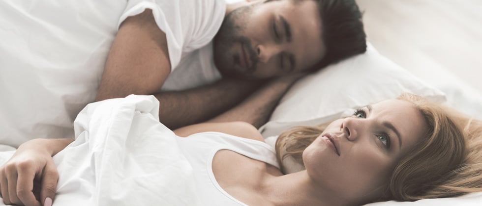 Couple in bed with the man sleeping and woman lying there thinking