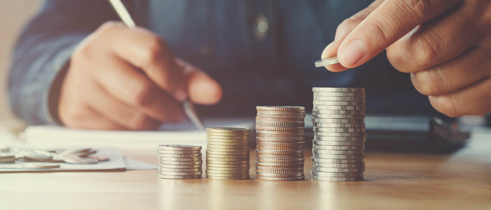 Man sitting down and counting stacks of coins & recording it