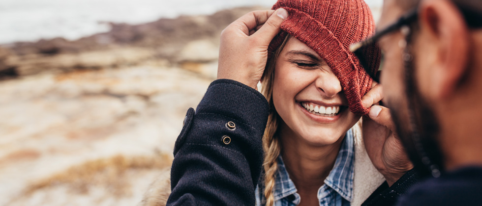 Playful guy pulling his girlfriend's hat over her face as she laughs