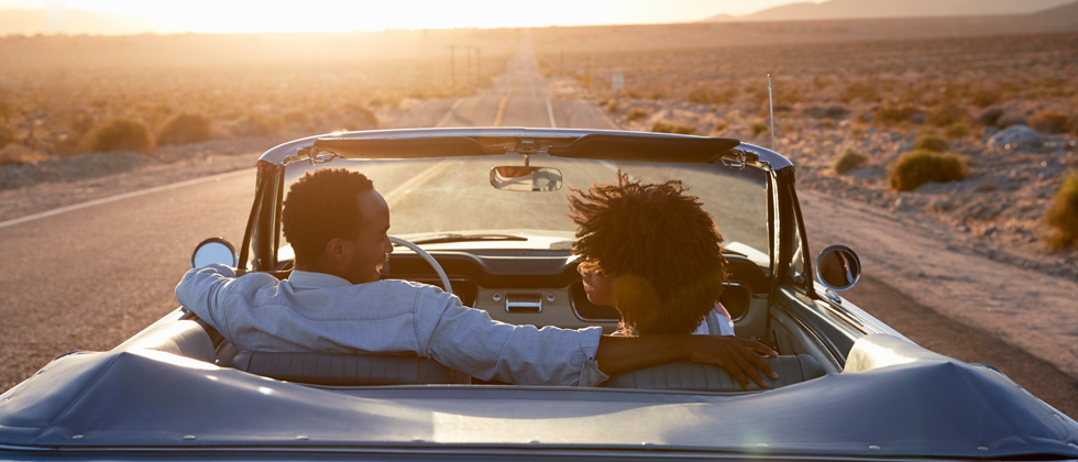 Couple driving through a desert road in a vintage convertible