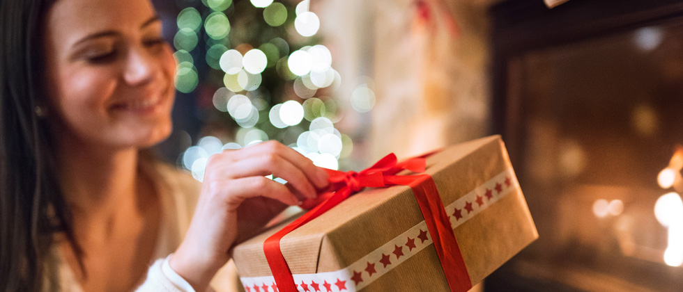 Woman happily opening a holiday gift next to the tree