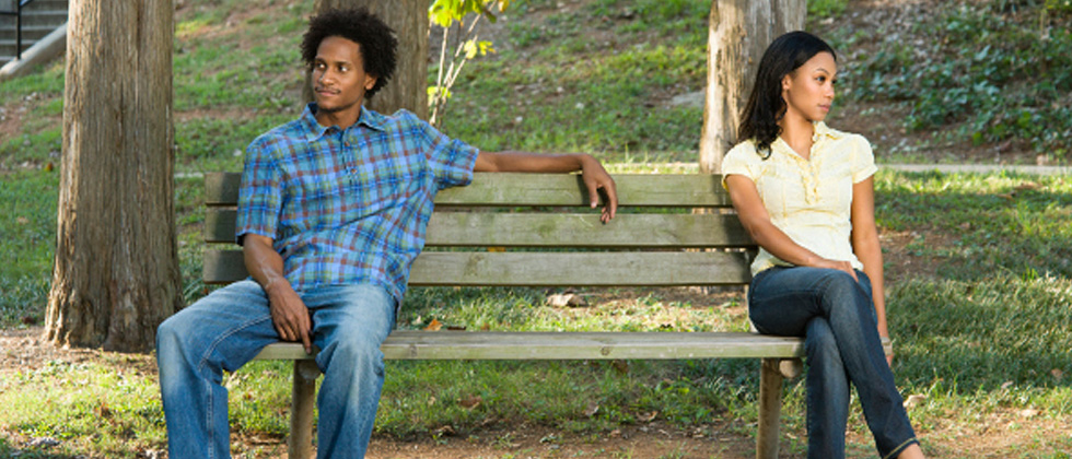 Couple sitting on a bench with a huge space between them looking away