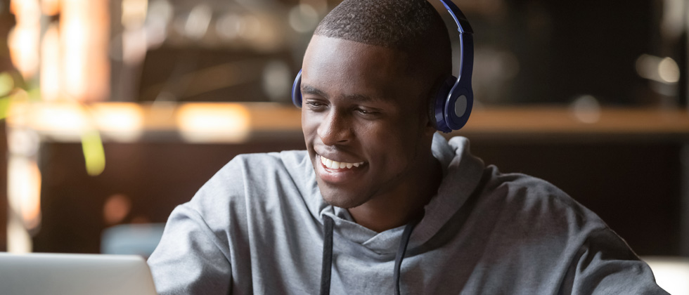 A guy sitting at his laptop smiling with headphones on