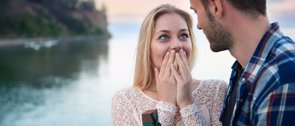 A woman being proposed to by her boyfriend in a romantic beach setting