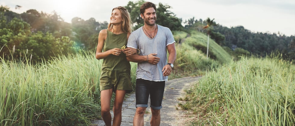 Couple walking along a scenic path while holding hands & smiling