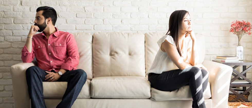 A couple on separate ends of a couch with their backs to each other