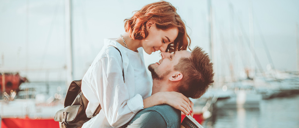 A man holding up a woman as she kisses him on a dock