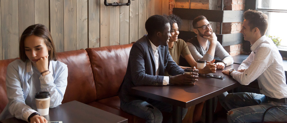 A group of friends having coffee with a sad girl sitting alone to the side