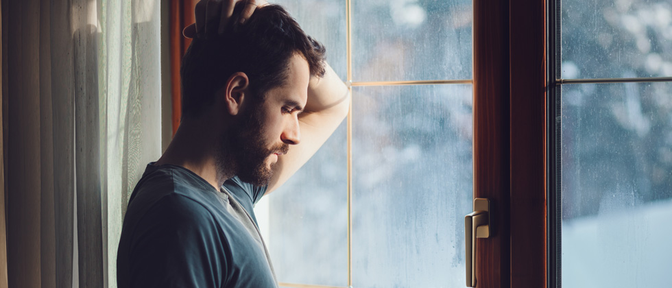 Man sadly looking out a rainy window in deep thought