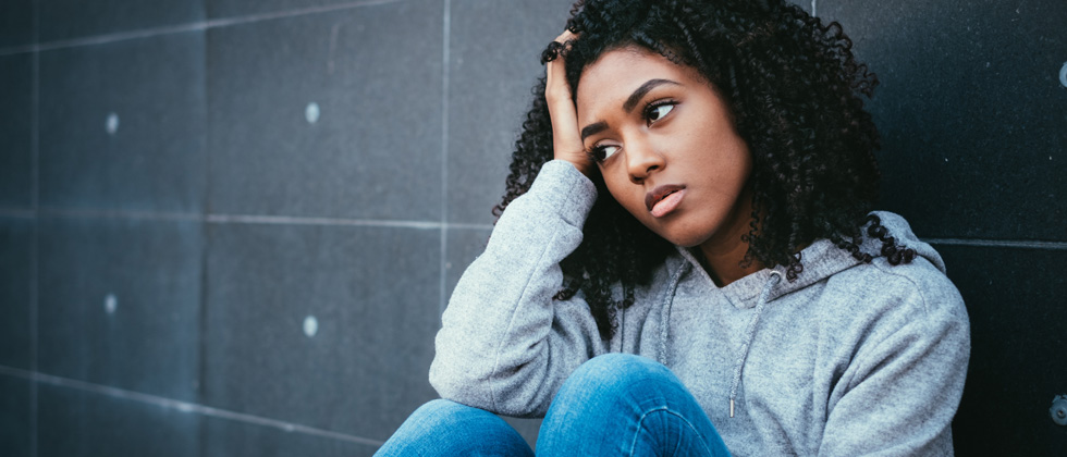 A woman sitting against a wall looking sad and confused