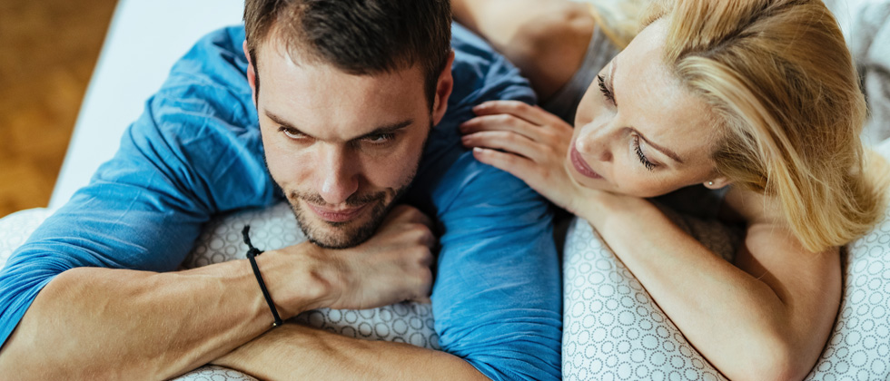 Man laying down and woman laying next him comforting him
