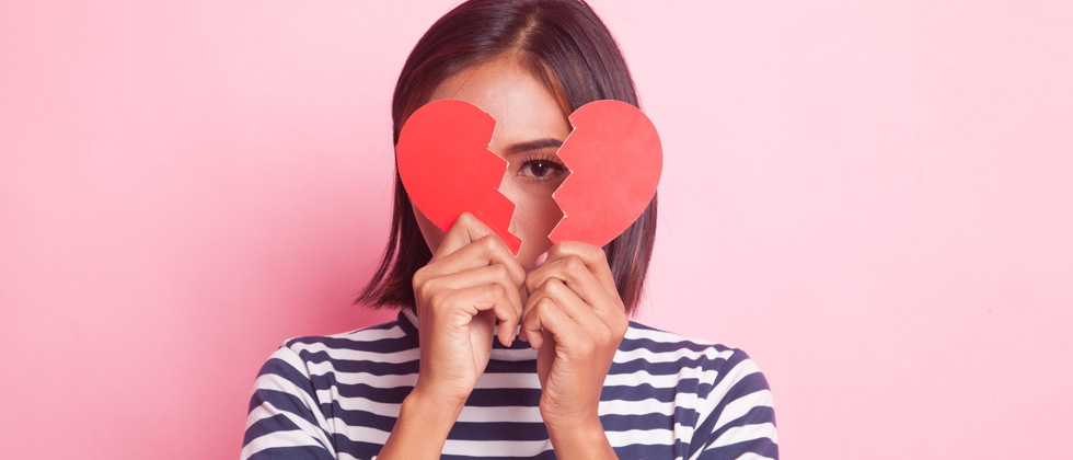 A woman holding a broken heart cutout over her face