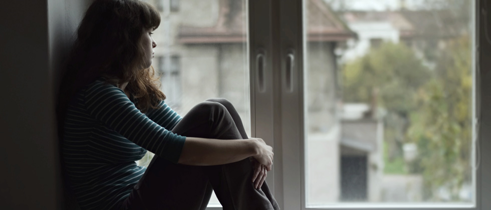 A woman looking upset and sitting on a window ledge staring out