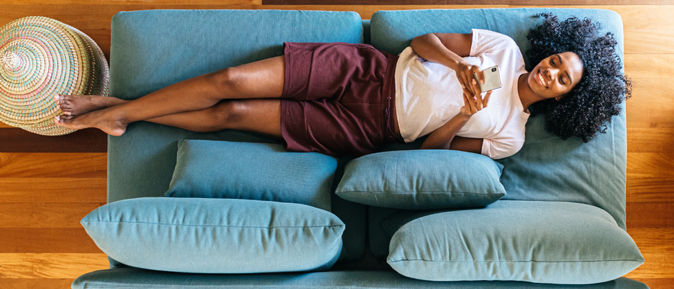 A woman laying on her couch smiling into her phone