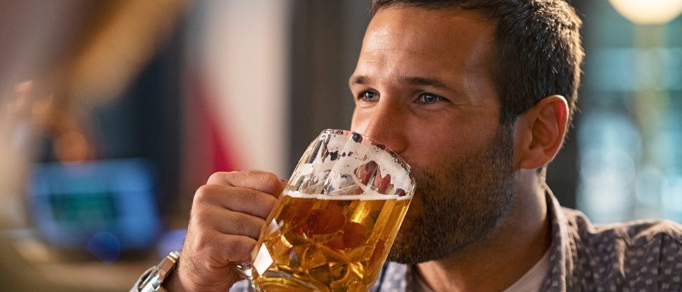 A guy happily drinking a huge beer at a bar