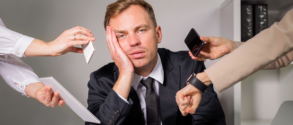 A guy looking exhausted with phones, papers & watches in front of him