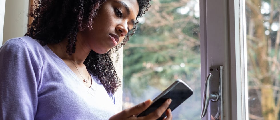 A woman standing at the door looking solemnly into her phone