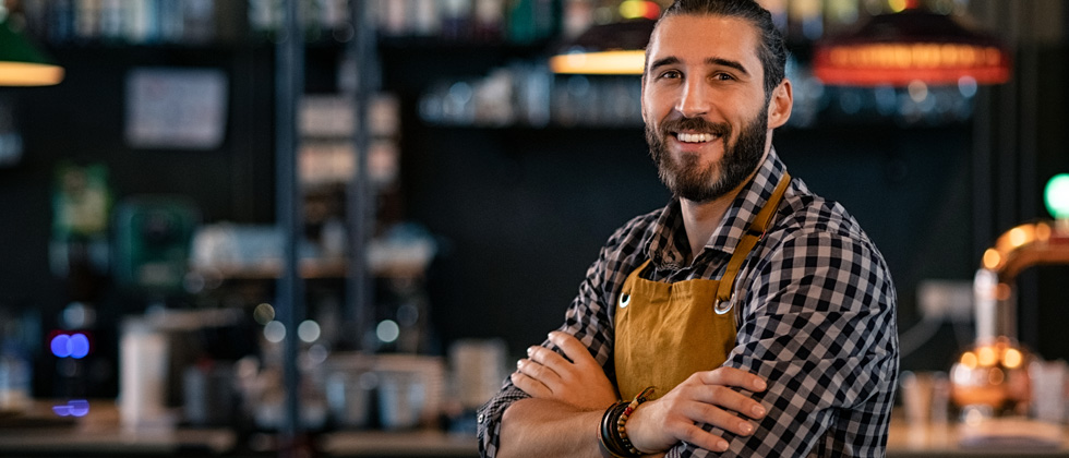 A guy leaning against a bar in his bartender uniform