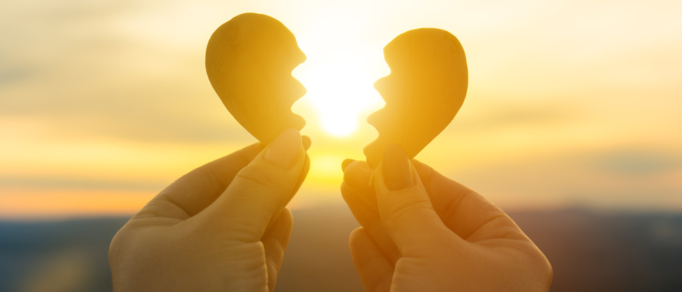 A broken cutout heart being pulled apart in front of a setting sun