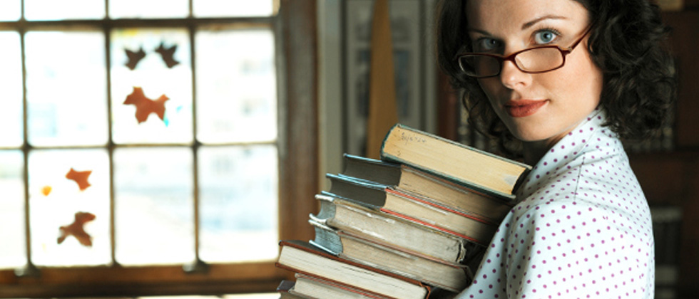 A woman wearing glasses holding a stack of books
