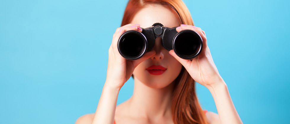 A woman holding up binoculars looking into the camera