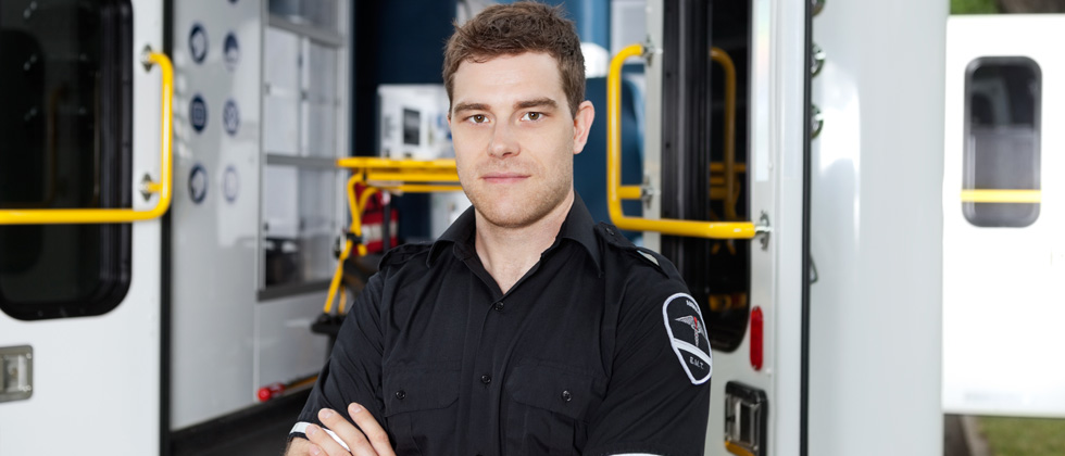 A male paramedic standing in uniform outside an ambulance