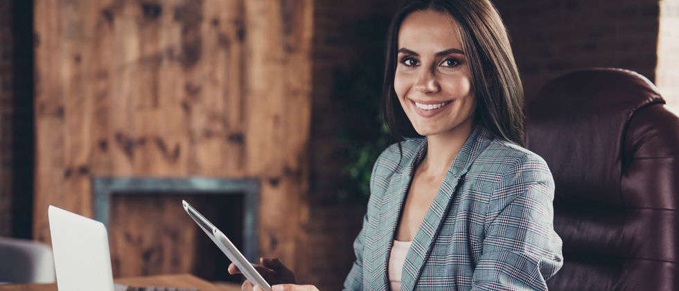 A woman in a suit sitting at her desk with an iPad on hand