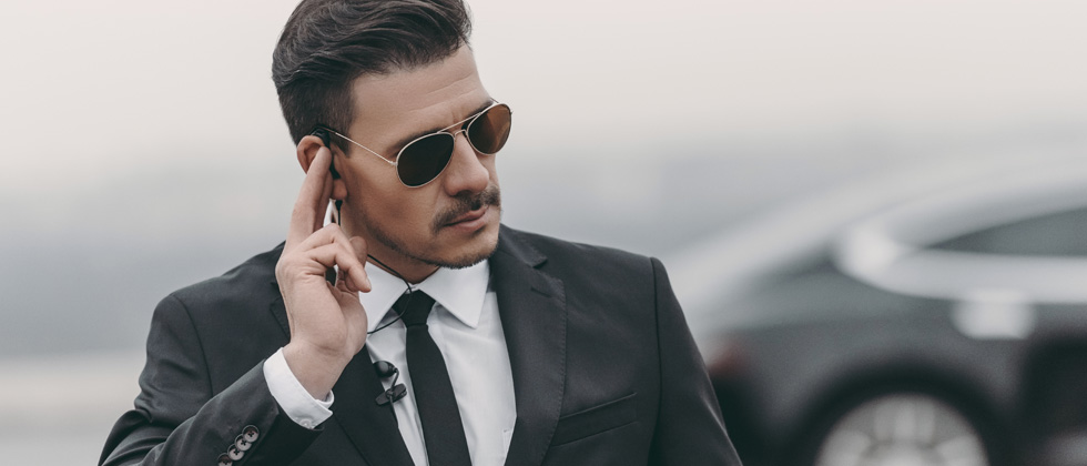 Male in a black suit with sunglasses listening to his ear piece