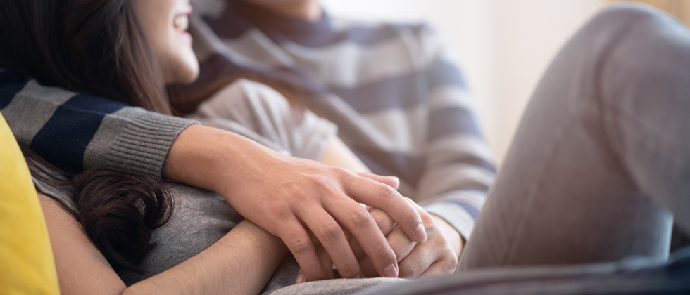 A couple cuddling on the couch holding hands